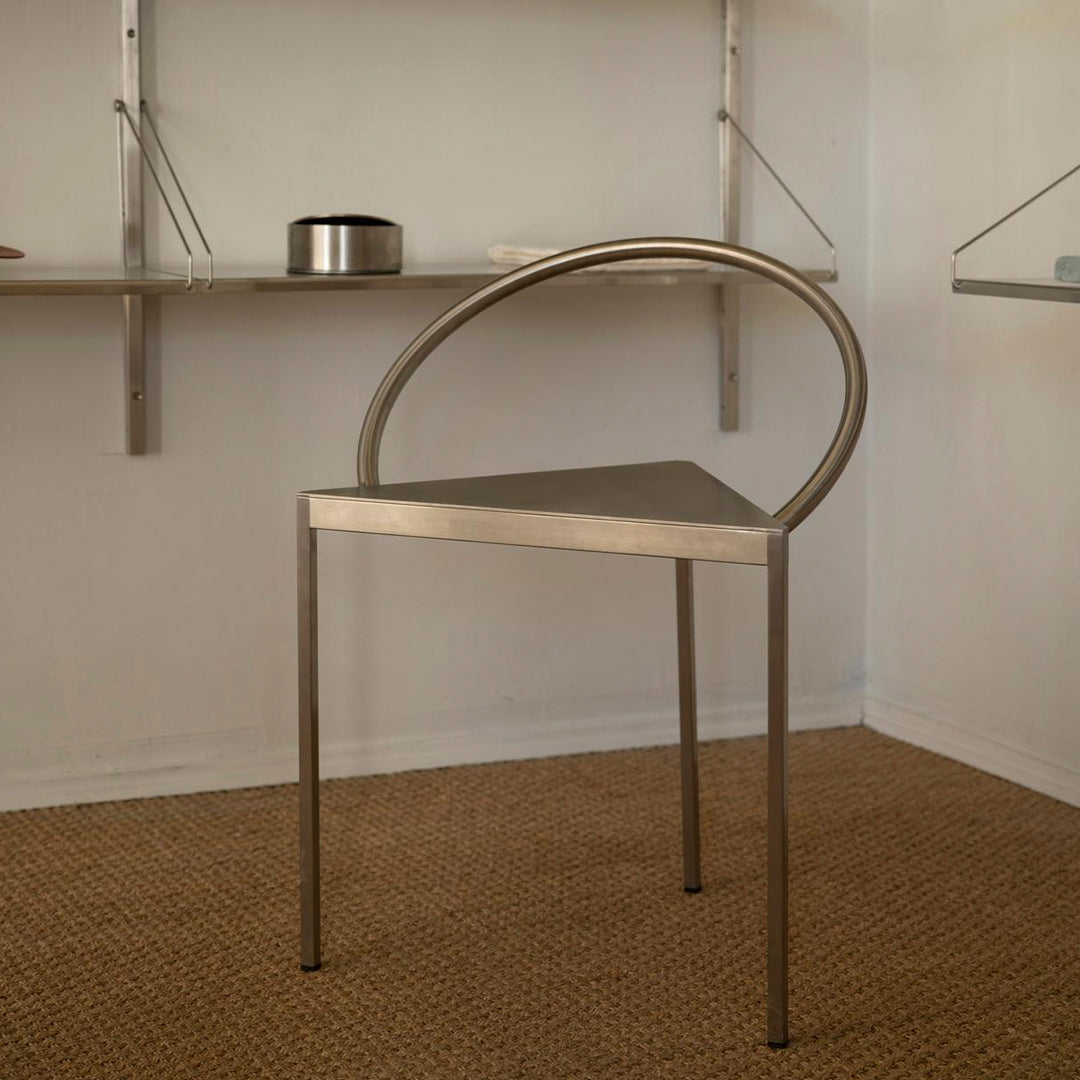 Sleek silver chair with a minimalist design and a geometric pattern, featuring a curved back and triangular seat.