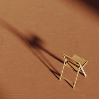 Light wooden folding chair on a warm, earthy brown backdrop with soft shadows creating depth.