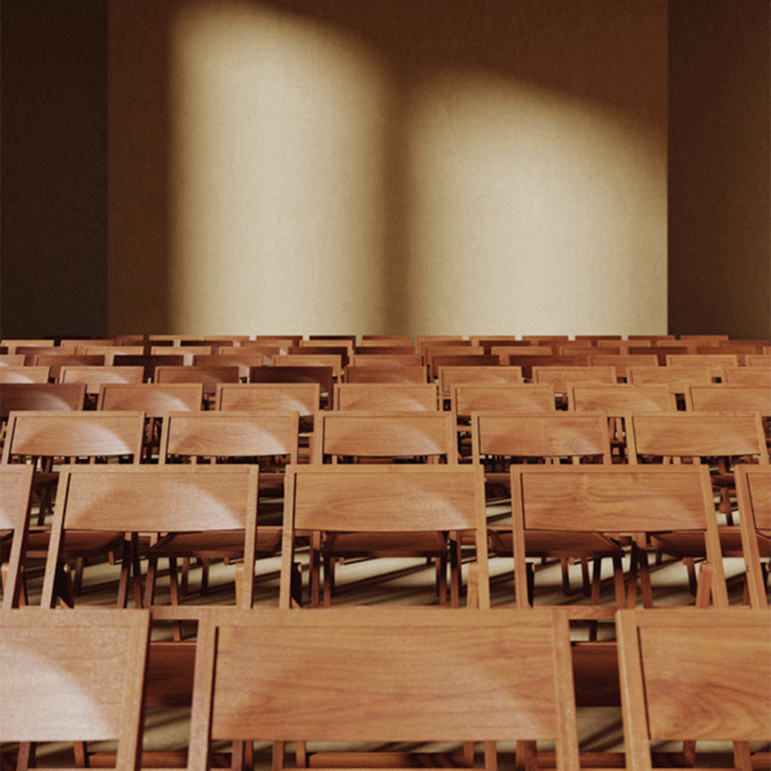 Rows of wooden chairs arranged in a warm, neutral-toned setting with soft lighting creating subtle shadows.