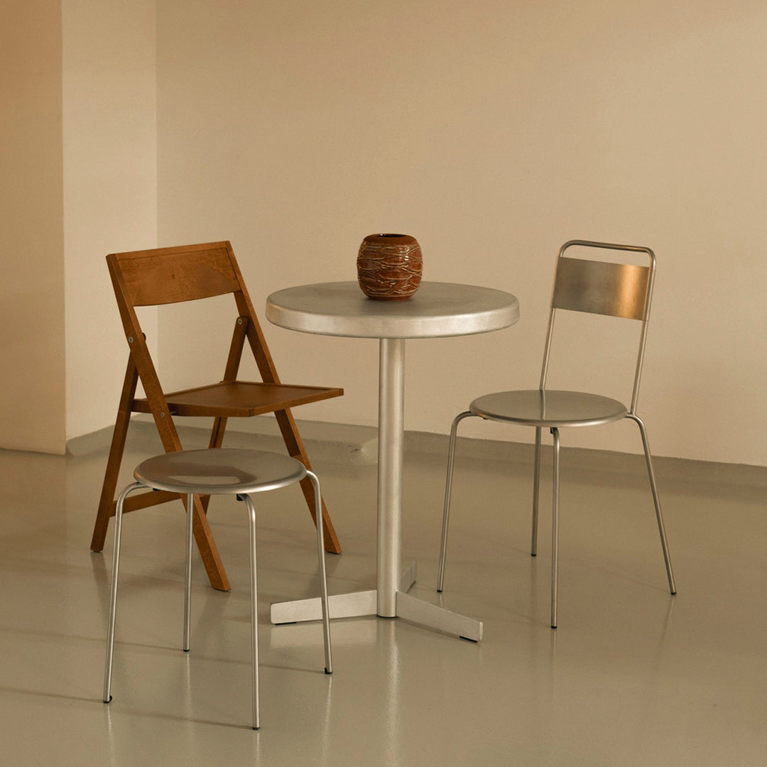 Metallic silver table with wooden and metal chairs against a soft beige background, creating a modern minimalistic look.