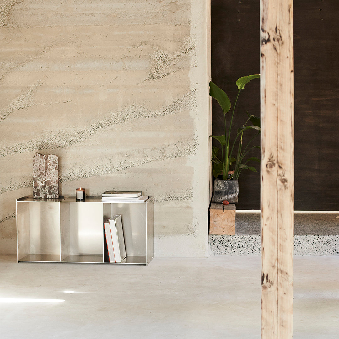Modern silver console table against a textured beige wall with earthy tones and natural wood accents.
