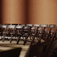 Row of black folding chairs against warm brown walls, featuring smooth wood texture and clean lines.
