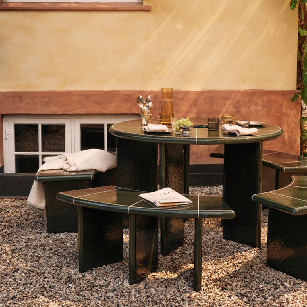 Round green table with matching benches, featuring sleek lines and a glossy finish, set on a gravel surface.