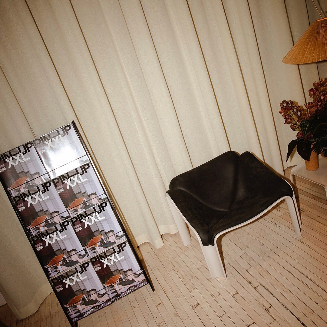 Black minimalist chair next to a patterned magazine display and beige curtains for a modern interior feel.