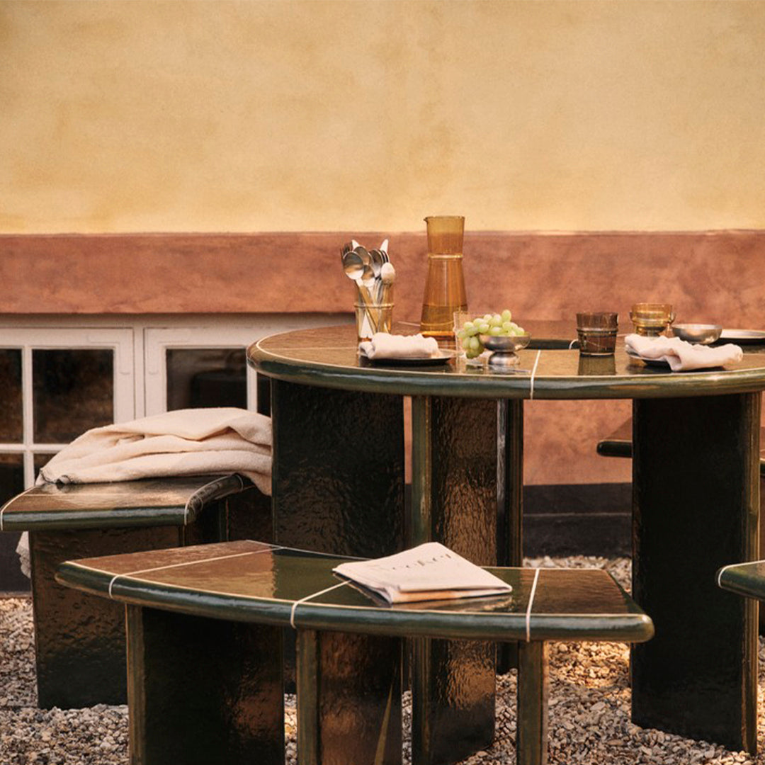 Green table and stools with a glossy finish, accented by subtle lighter lines, set against a warm, earthy background.
