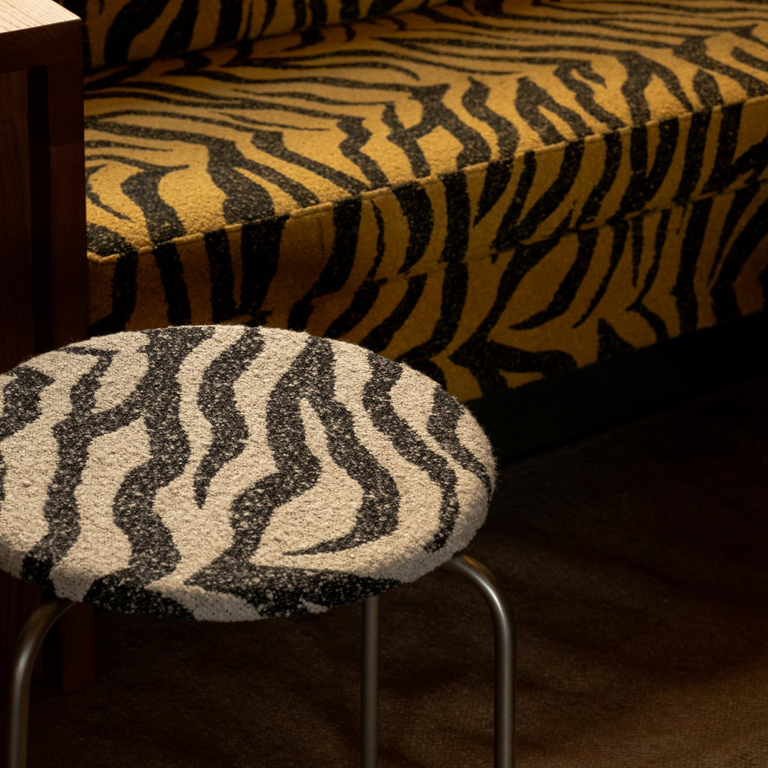 Yellow and black tiger stripe sofa with a round gray and white stripe stool. Bold patterns add a wild touch to decor.