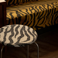 Yellow and black tiger stripe sofa with a round gray and white stripe stool. Bold patterns add a wild touch to decor.