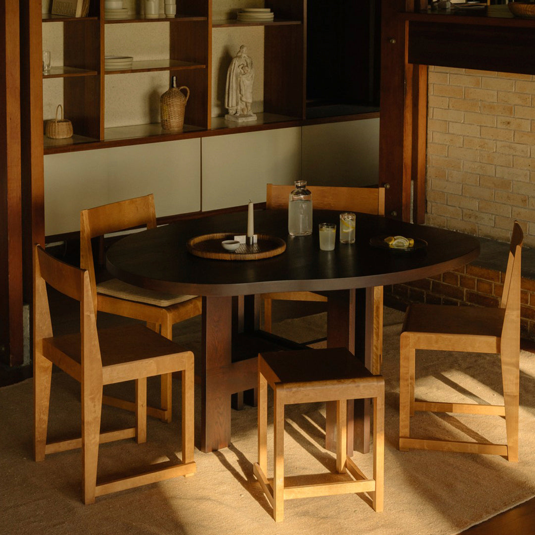 Modern round black dining table with light wood chairs in a warm, minimalist interior setting. Perfect for contemporary homes.