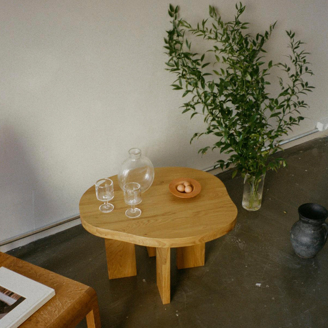 Natural wooden coffee table with a light oak finish, simple lines, and a minimalist design. Accented by greenery.
