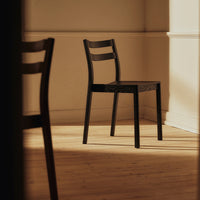 Black wooden chair with a minimalist design, featuring smooth lines and a sleek finish against a warm light backdrop.