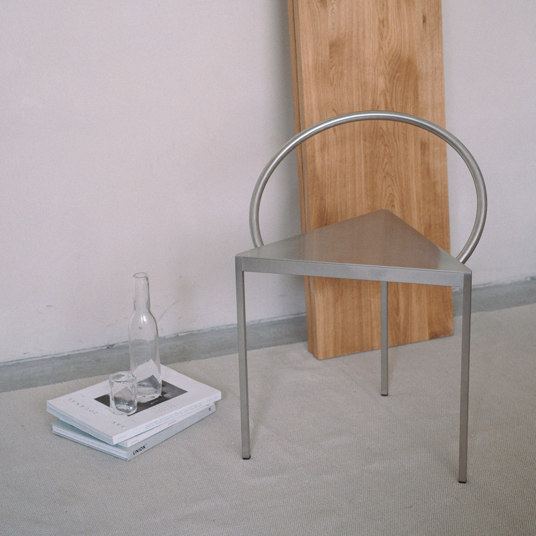Sleek silver triangle chair with round back, paired with natural wood accent, set against a light gray backdrop.