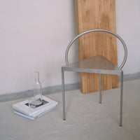 Sleek silver triangle chair with round back, paired with natural wood accent, set against a light gray backdrop.