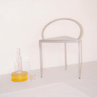 Silver transparent chair with a modern circular design, accompanied by clear and yellow glass vases on a neutral background.
