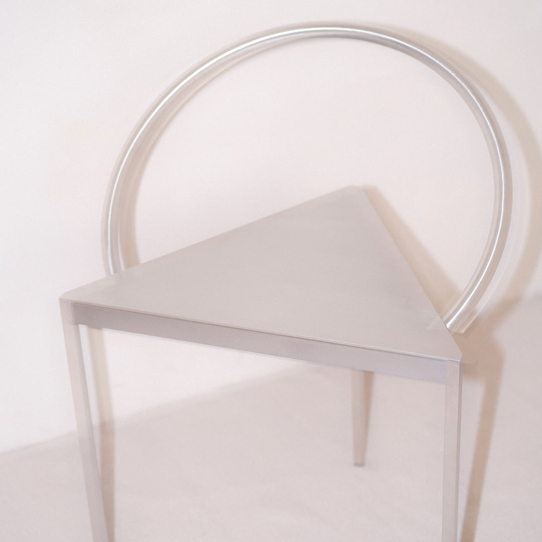 Silver triangular chair with a circular backrest, featuring a sleek, modern design and minimalist aesthetic.