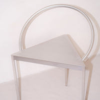 Silver triangular chair with a circular backrest, featuring a sleek, modern design and minimalist aesthetic.