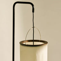 Black metal stand with a cream-colored cylindrical shade and gold detailing, showcasing minimalistic elegance and soft hues.