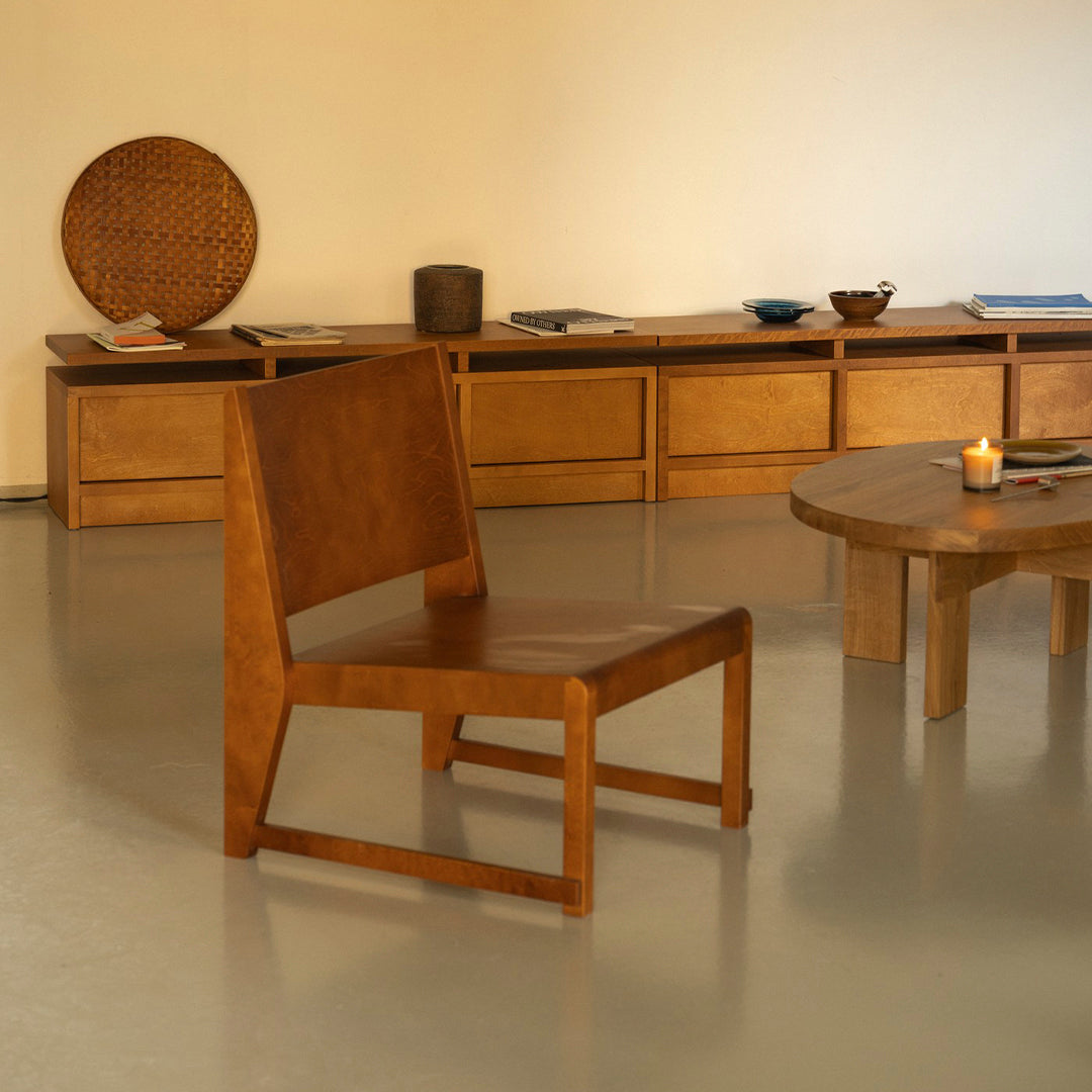 Natural wood color chair with a sleek geometric design, set against a minimalist, warm-toned interior.