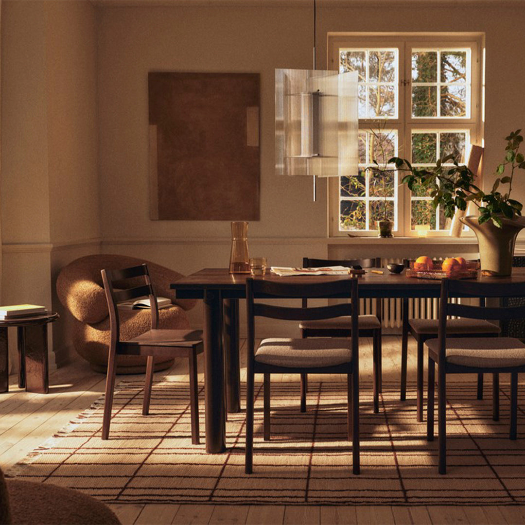 Warm beige walls with natural light, dark wood table, neutral-toned chairs, and a patterned beige rug.