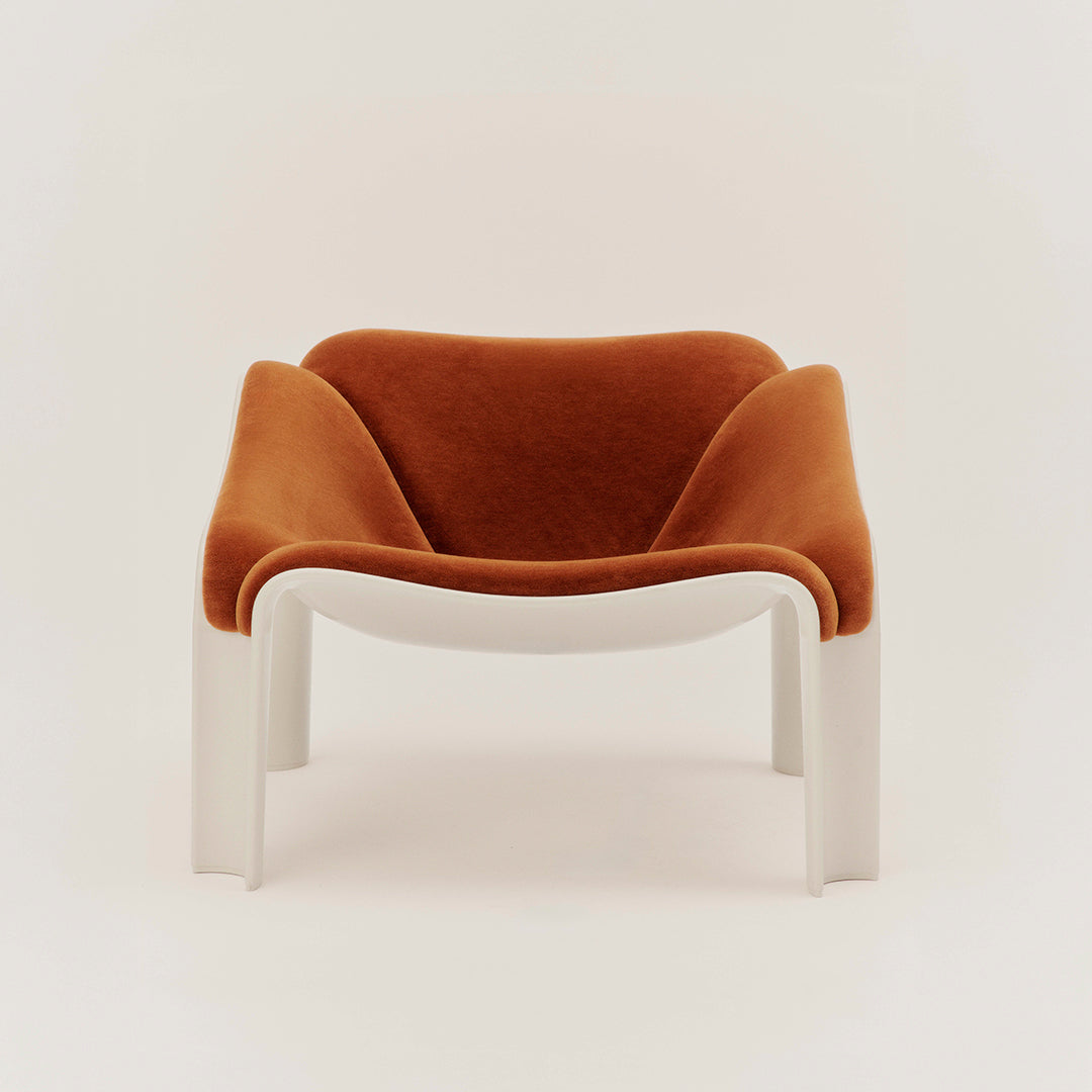 Rust-colored velvet armchair with smooth white legs, featuring modern ergonomic design and minimalistic style.