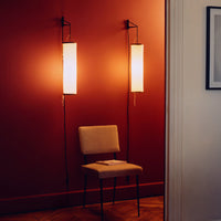"Modern wall sconces with warm glow against a deep red wall, featuring a simple beige chair for contrast."