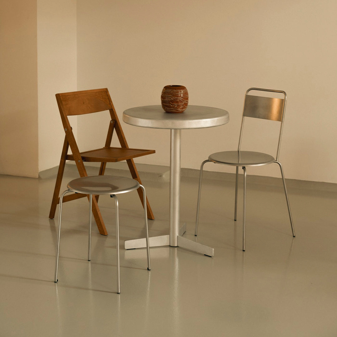 Modern seating set featuring a wooden chair, silver metal chairs, and a round aluminum table on a light floor.