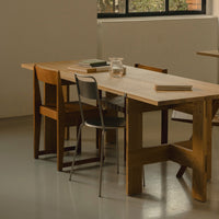 Wooden table with a light natural finish, complemented by brown and gray chairs. Minimalist design with clean lines.