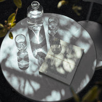 White book with striped pattern, glass water bottle, and clear glasses casting soft shadows on a round table.