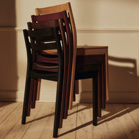 Stacked wooden chairs in varying shades of black, brown, and natural wood, showcasing smooth finishes and simple lines.