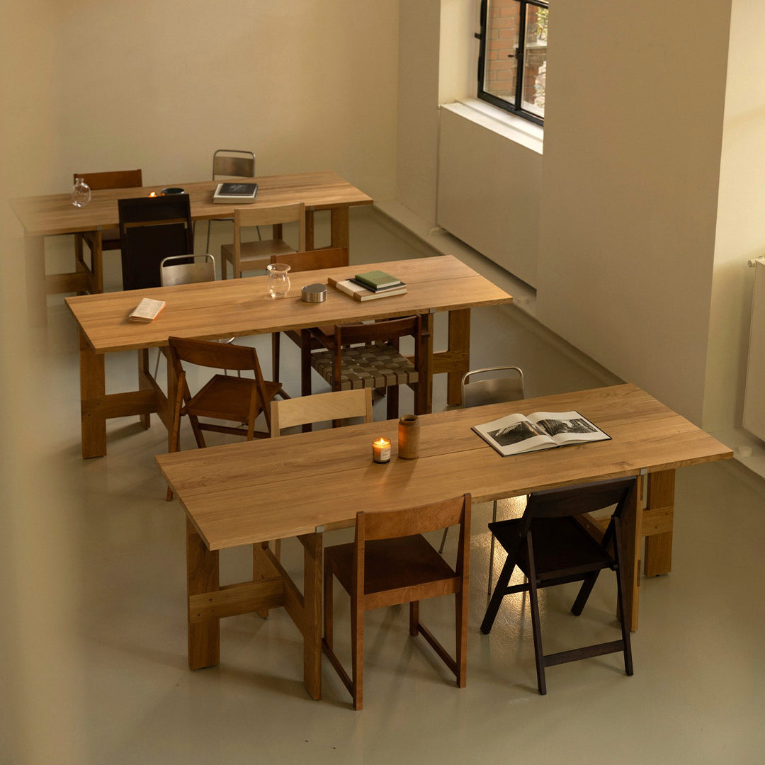 Light wood tables with natural finishes and contrasting dark wooden chairs in a minimalist, cozy workspace setting.