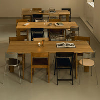 Wooden tables with natural finish and various colored chairs, including silver, black, and light beige, create a stylish pattern.