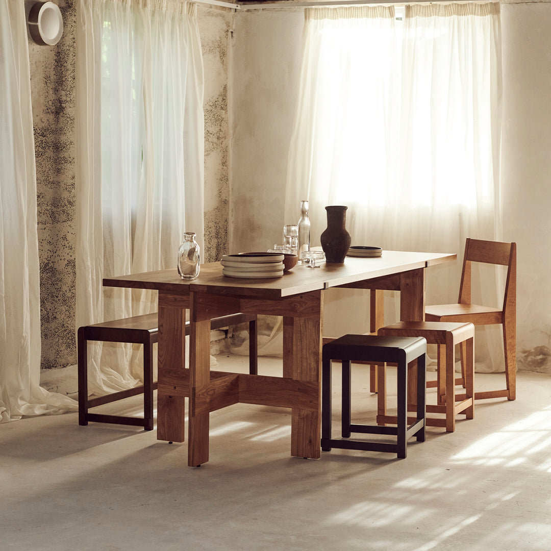 Wooden dining table with a natural finish, paired with black and wooden chairs, set against a light, airy background.