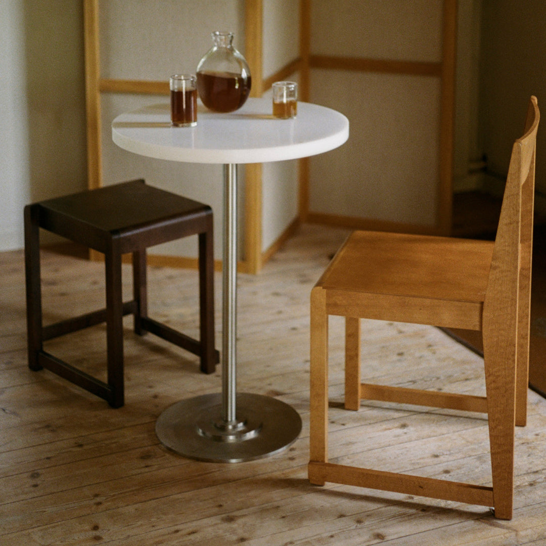 Modern round white table with stainless steel base, complemented by dark brown and light wooden chairs.