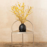Black vase with yellow branches on a sleek metallic table against a soft beige background. Modern and stylish decor.