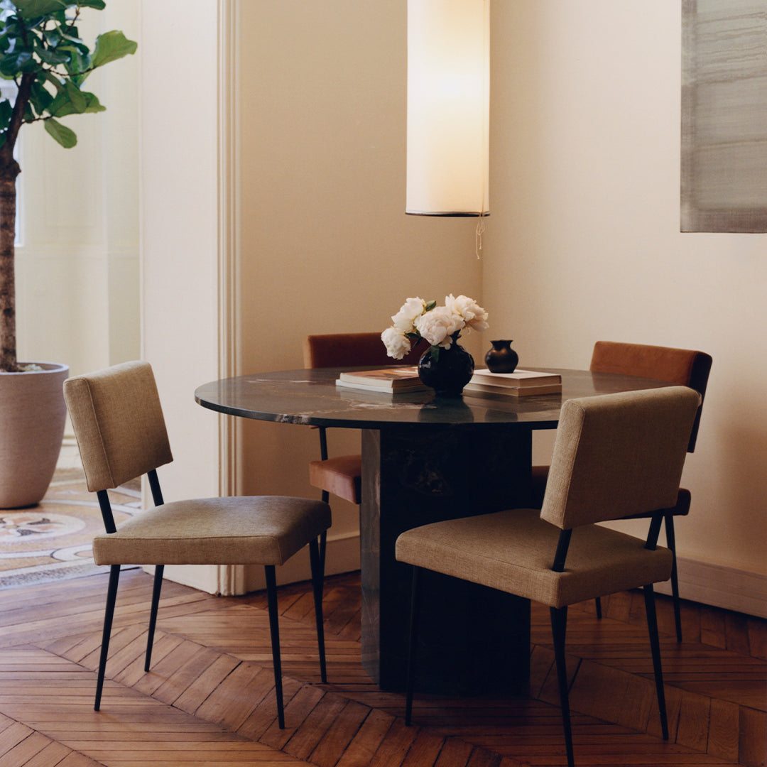 Stylish round table with a marble top and neutral-toned chairs, set against a warm wooden floor and soft lighting.
