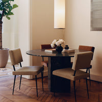 Stylish round table with a marble top and neutral-toned chairs, set against a warm wooden floor and soft lighting.