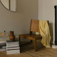 Wooden chair with a yellow draped fabric, stacked white books, and a brown vase in a neutral-toned room.