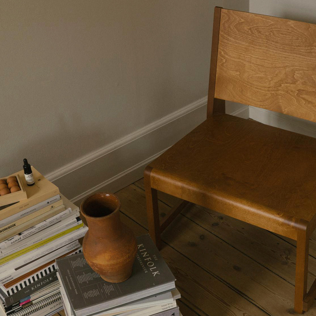 "Natural oak chair with smooth, warm wood finish beside a terracotta vase and stacked books, set in neutral tones."