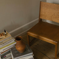"Natural oak chair with smooth, warm wood finish beside a terracotta vase and stacked books, set in neutral tones."