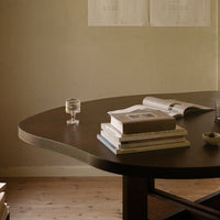 Curved dark wood table with stacked books and a glass, featuring warm neutral tones and minimalist design.
