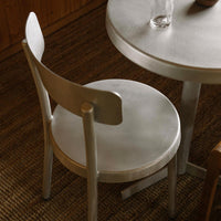 Sleek silver metal chair with a round table, featuring a minimalist design and smooth, understated finishes.