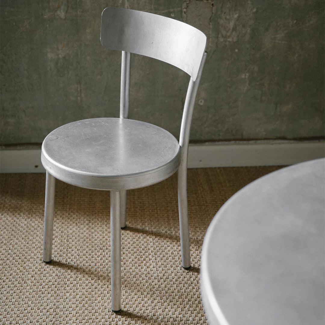 Silver metal chair with a smooth, sleek finish against a textured neutral background.