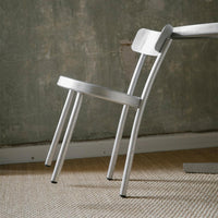 Silver metal chair with a sleek, modern design against a textured gray wall and woven beige rug.
