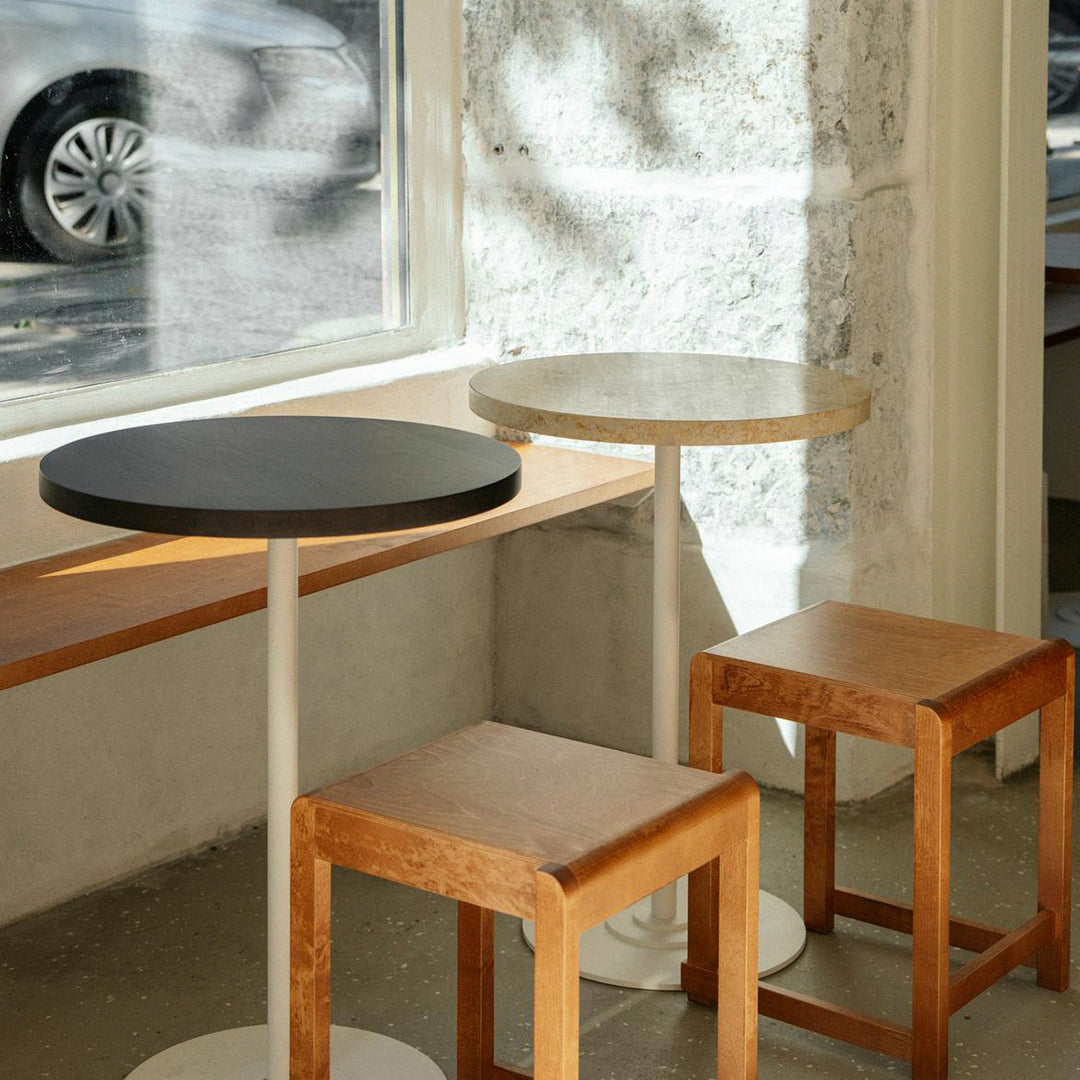 Three modern tables: one black circular top, one light-colored round top, and two wooden square stools.