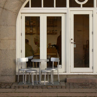 Silver metal chairs and table set against a light cream-colored entrance, with a hint of rustic stone texture.
