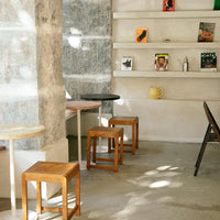"Set of wooden stools in natural tones with minimalist design, against a textured gray wall and shelves."