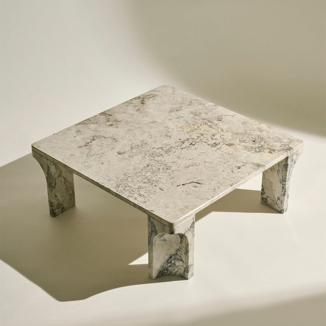 Marble square coffee table featuring a light beige surface with gray and white veining, highlighted by textured legs.