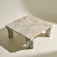 Marble square coffee table featuring a light beige surface with gray and white veining, highlighted by textured legs.