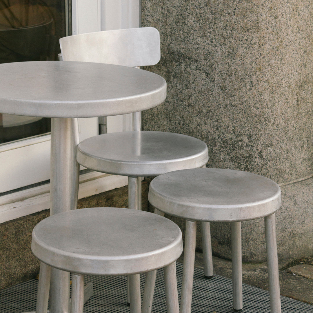 Metallic silver round table and stools with a sleek, minimalist design. Perfect for modern outdoor settings.