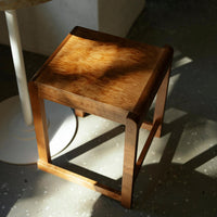 Natural wood stool with a warm honey finish and subtle grain patterns, casting soft shadows on a light floor.