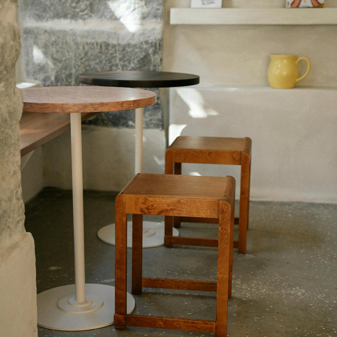Wooden and black stools beside a round pink-top table with a white base against a textured gray background.